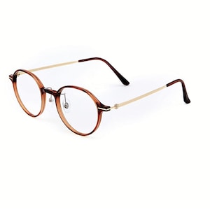 May include: Round eyeglasses featuring a translucent brown acetate frame with a thin gold-tone metal bridge and temples. The temples transition into dark brown acetate tips. The clear lenses are held by a thin rim with adjustable nose pads.