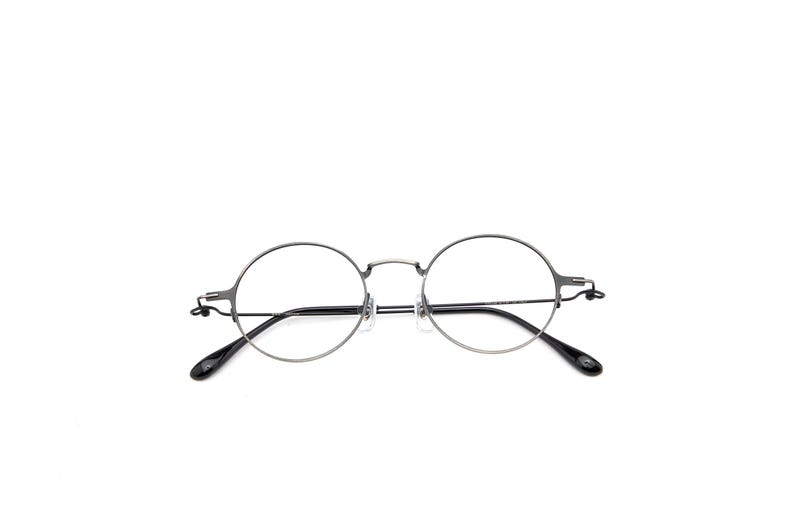 May include: Round eyeglasses featuring a thin, dark metallic frame with a bridge and adjustable nose pads. The temples are slender with black acetate tips, providing a clean and functional design for these circular spectacles with clear lenses.