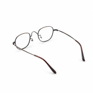 May include: A pair of eyeglasses with a thin, dark metal frame and clear lenses. The temples are a dark brown color. The glasses are set against a white background.