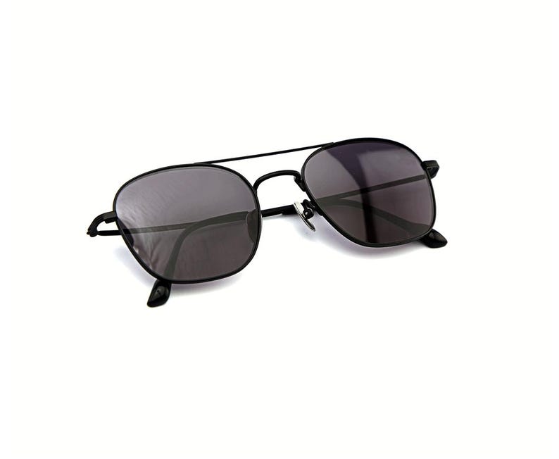 May include: Black metal frame sunglasses featuring a double bridge design and dark tinted lenses. The eyewear has a thin, lightweight construction with adjustable nose pads and curved temple tips, providing a classic look with a modern aesthetic.