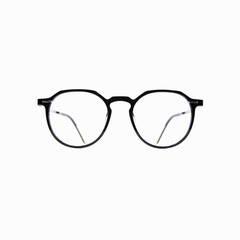 May include: Black-framed eyeglasses with a round shape. The glasses have clear lenses and thin, silver-colored arms. The frame is made of a matte black material. The overall design is minimalist and modern.