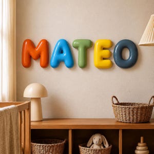 May include: A set of five glossy, three-dimensional wall-mounted letters spelling the name MATEO. The letters are colored orange, blue, green, yellow, and dark gray, featuring a smooth, rounded, balloon-like appearance mounted on a plain wall.