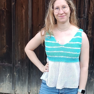 Könnte beinhalten: Ärmelloses Top mit türkisfarbenen und weißen Streifen und einem weißen, offen gewebten Unterteil. Das Top mit V-Ausschnitt wird mit einer blauen Jeans kombiniert. Der Hintergrund ist eine verwitterte Holztür.