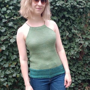 Könnte beinhalten: Ein grünes Neckholder-Top mit dunklerem grünen Besatz und Trägern. Das Top wird mit einer blauen Jeans kombiniert. Die Frau auf dem Bild trägt eine Sonnenbrille und steht vor einem grünen, belaubten Hintergrund.