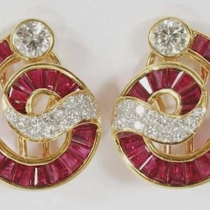 May include: A pair of gold earrings featuring a spiral design set with baguette-cut red rubies and round brilliant-cut white diamonds. Each earring has a single large round diamond at the top and a curved band of pavé-set diamonds across the centre.