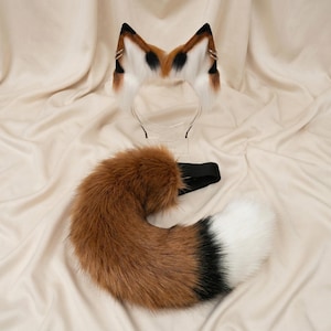 Op de afbeelding: Een vossenkostuumset met een hoofdband met oren en een staart. De oren zijn wit met bruine en zwarte punten, en de staart is bruin met een witte punt en zwart accent. Voor cosplay of kostuums.