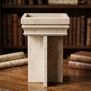 Può includere: Un piedistallo in pietra beige con una parte superiore quadrata e una base a forma di croce. La struttura presenta una consistenza liscia e screziata con variazioni naturali di colore, mostrando un design architettonico pulito con un bordo.