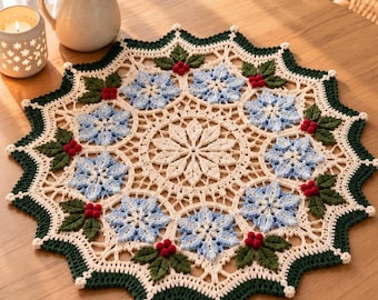 May include: A round, crocheted doily featuring a central cream-colored star motif surrounded by light blue snowflake patterns. The border is accented with dark green leaves and small red berries, finished with a scalloped dark green edge.