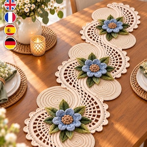 Puede incluir: Un camino de mesa de ganchillo de color crema con un intrincado patrón de celosía sinuoso y bordes festoneados. El camino está decorado con flores tridimensionales de color azul claro con centros marrones y hojas verdes texturizadas.