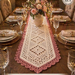 Puede incluir: Una elegante mesa de comedor con un camino de mesa de ganchillo color crema con un borde festoneado rosa. La mesa está decorada con platos con borde dorado, copas de cristal y un centro de mesa floral. El texto "Elegant Dining Setup" es visible.