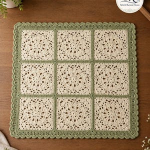 Könnte beinhalten: Ein quadratisches Häkeldeckchen mit neun cremefarbenen Blumenmotiven in einem Raster, die mit salbeigrünem Garn umrandet und getrennt sind. Die Kanten sind mit einer gewellten Häkelborte versehen. Ein rundes Logo zeigt den Text Stitch Runner Store.