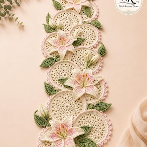 May include: A handmade crochet table runner featuring cream-coloured doilies with pink scalloped edges. Each doily is decorated with a pink and white lily flower and green leaves. The runner is a decorative home accent, perfect for a dining table.