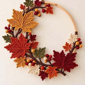 Puede incluir: Un adorno de pared circular con un aro de bambú decorado con hojas de arce tejidas a ganchillo en tonos rojo, naranja, amarillo, verde y crema. El diseño incluye ramas tejidas en marrón y pequeños racimos de bayas redondas rojas y amarillas.