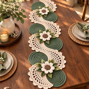 Peut inclure: Un long chemin de table décoratif présentant un motif au crochet avec une alternance de cercles vert foncé et de sections en dentelle festonnée crème. Des fleurs en relief crème à cœur marron et feuilles vertes sont fixées.