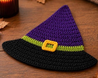 May include: A crocheted witch hat featuring a purple pointed crown, a black brim, a lime green band, and a yellow square buckle. The item is flat and textured with visible yarn stitches, showcasing a vibrant color palette of purple, black, green, and yellow.