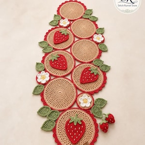 May include: A handmade crochet table runner with a strawberry design. The runner has a beige centre with a red scalloped edge, decorated with red strawberries, green leaves, and white flowers. The runner is approximately 76 cm long.
