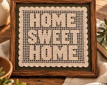 Könnte beinhalten: Ein quadratischer Holzrahmen mit einer cremefarbenen Häkeldecke mit gewelltem Rand. Die Häkeldecke zeigt den Text HOME SWEET HOME in einer Blockschrift vor einem dunkelgrünen Hintergrund innerhalb des Rahmens.