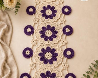 May include: A long, rectangular crochet table runner featuring a repeating pattern of five large, cream-colored floral motifs with deep purple petals, connected by smaller cream-colored circular accents and tiny flower shapes. The text SR Stitch Runner Store is visible in the top right corner.