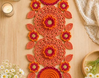 Könnte beinhalten: Ein rechteckiger Häkel-Tischläufer mit einem sich wiederholenden Muster aus großen orangefarbenen runden Deckchen, kleineren Blumenmotiven in Orange, Pink und Gelb sowie blattförmigen Akzenten in Orange, die vertikal angeordnet sind.