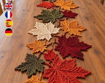 Könnte beinhalten: Ein gehäkelter Tischläufer mit einer Reihe miteinander verbundener Ahornblätter in den Farben Rot, Orange, Gelb, Creme und Olivgrün. Die Blätter sind in einem rankenartigen Muster angeordnet und zeigen durchgehend detaillierte Maschenstrukturen.