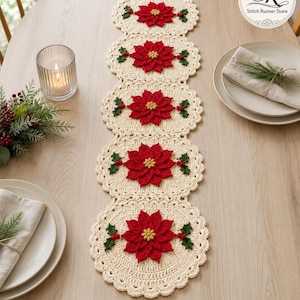 May include: A cream-colored crocheted table runner featuring five circular sections, each decorated with a central red poinsettia flower, green leaves, and small red berries. The runner has a scalloped edge and a delicate, intricate stitch pattern.