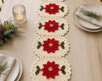 May include: A cream-colored crocheted table runner featuring five circular sections, each decorated with a central red poinsettia flower, green leaves, and small red berries. The runner has a scalloped edge and a delicate, intricate stitch pattern.