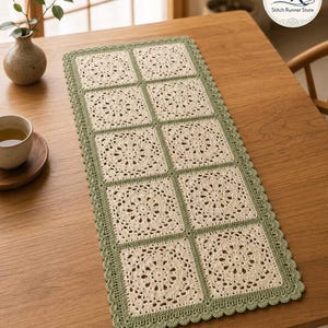 Pode incluir: Um caminho de mesa retangular de crochê com oito motivos quadrados na cor creme com padrões florais intrincados, unidos e contornados por fio verde sálvia. As bordas do caminho são finalizadas com um acabamento de crochê festonado.