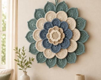 May include: A circular crochet wall hanging featuring a layered floral design in shades of teal, cream, and blue. The piece has a central cream flower, surrounded by concentric rings of blue, cream, and teal petals, with a loop for hanging.