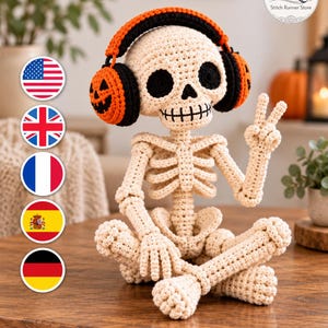 May include: A crocheted skeleton figurine in an off-white yarn, sitting cross-legged and making a peace sign with one hand. The skeleton wears black and orange headphones with a jack-o'-lantern face design on the ear cups and black eye sockets.