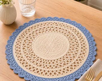 Può includere: Un sottopentola rotondo all'uncinetto color crema con un bordo smerlato blu chiaro. Il sottopentola presenta un motivo traforato ed è posto su un tavolo di legno. Un bicchiere d'acqua, un vaso con fiori e posate sono anche sul tavolo.