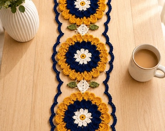 May include: A long, rectangular crochet table runner featuring three large, circular floral motifs in shades of mustard yellow, navy blue, and white. The runner has a scalloped navy blue border and small green leaf accents between the flowers.