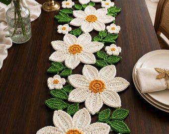 May include: A crochet table runner featuring a repeating pattern of large white daisy flowers with yellow centers and smaller white flowers, interspersed with green crocheted leaves. The design is arranged in a linear, floral-inspired motif.