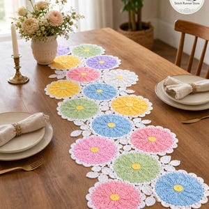 Puede incluir: Camino de mesa de ganchillo hecho a mano con un diseño de margarita. El camino de mesa muestra una serie de flores circulares vibrantes en tonos pastel de rosa, amarillo, azul, verde y morado, cada una con un centro amarillo y ribete blanco. Colocado sobre una mesa de madera.