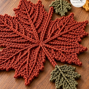 May include: A large, rust-coloured crocheted maple leaf with prominent textured veins, accompanied by two smaller olive green crocheted leaves attached by stems. A circular logo in the corner displays the text SR Stitch Runner Store.
