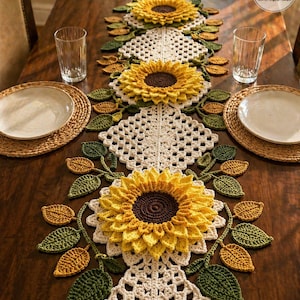 May include: A handcrafted crochet table runner featuring three large sunflowers with yellow petals and brown centers. The runner includes cream-colored openwork squares and green and gold leaves, creating a floral design. The runner is placed on a dark wooden table.