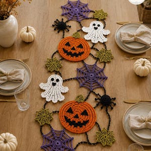 May include: A Halloween-themed crochet table runner featuring orange pumpkins with black faces, white ghosts, purple spiderwebs, green star-shaped motifs, and black spiders connected by a black crocheted chain, arranged in a decorative garland pattern.