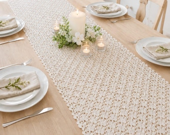 Könnte beinhalten: Cremefarbener Tischläufer mit offenem Gewebe und gewelltem Rand, auf einem hellen Holztisch. Der Läufer ist mit einer großen weißen Kerze, kleinen Teelichtern und floralen Akzenten dekoriert. Gedecke mit weißen Tellern und Leinen-Servietten sind sichtbar.
