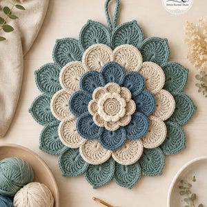 May include: A circular crochet potholder featuring a layered floral design in shades of teal, cream, and blue. The piece has a central cream flower, surrounded by concentric rings of blue and cream petals, finished with a teal outer border and a hanging loop. The logo "SR Stitch Runner Store" is visible in the top right corner.