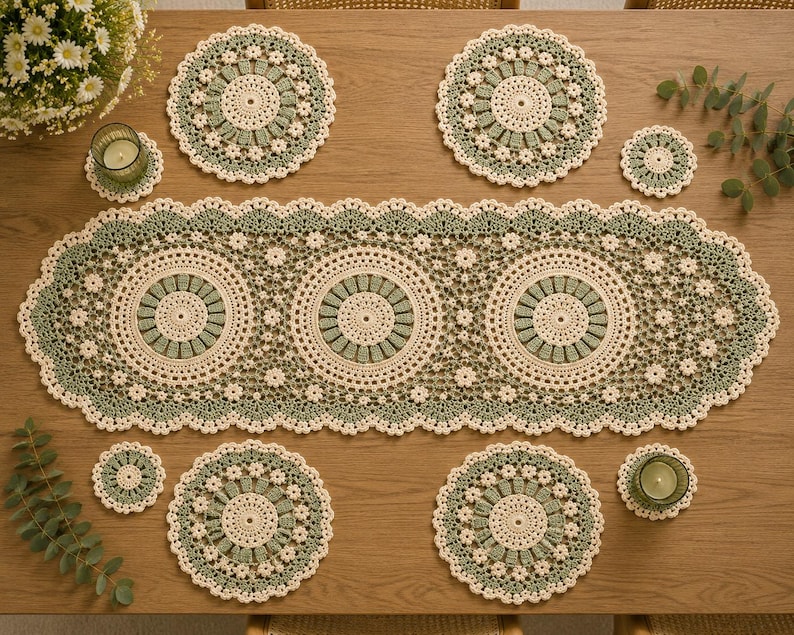 May include: A crochet table runner featuring three large circular motifs in cream and sage green, surrounded by a delicate floral lace border. The set includes four matching circular placemats and four small coasters in the same colour scheme.