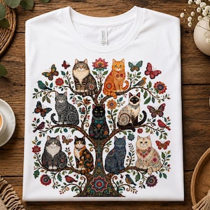 Może przedstawiać: Biały t-shirt z kolorowym nadrukiem graficznym przedstawiającym drzewo, na którego gałęziach siedzi osiem kotów różnych ras i maści, otoczonych skomplikowanymi wzorami kwiatowymi, liśćmi oraz kilkoma motylami i małymi ptakami.