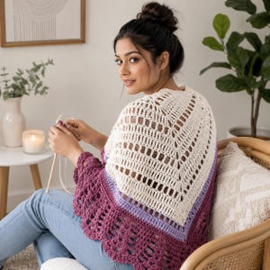 Può includere: Uno scialle all'uncinetto color crema con un motivo geometrico traforato, rifinito con un bordo viola e lavanda. Lo scialle è drappeggiato sulle spalle, mettendo in risalto gli intricati dettagli fatti a mano. Parte di una collezione di articoli all'uncinetto fatti a mano.