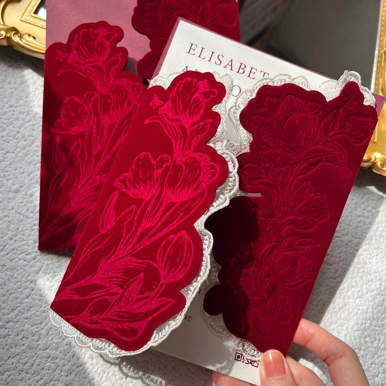 May include: Close-up of red velvet cards with a floral design and white lace trim. The cards have a tulip pattern embossed on the front. The word "ELISABETH" is visible on the card inside.