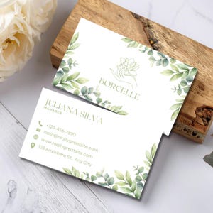 May include: Two white business cards featuring a green watercolor eucalyptus leaf border. One card displays the name BORCELLE with a line art icon of a hand holding a flower. The other card lists JULIANA SILVA, MANAGER, with contact details.