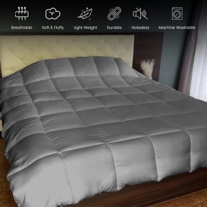 Op de afbeelding: Een grijze, gewatteerde dekbedovertrek op een bed. De dekbedovertrek is gemaakt van een zacht, donzig materiaal en is lichtgewicht. De dekbedovertrek is ademend, duurzaam en machinewasbaar. Het bed heeft een beige hoofdbord en staat in een slaapkamer.