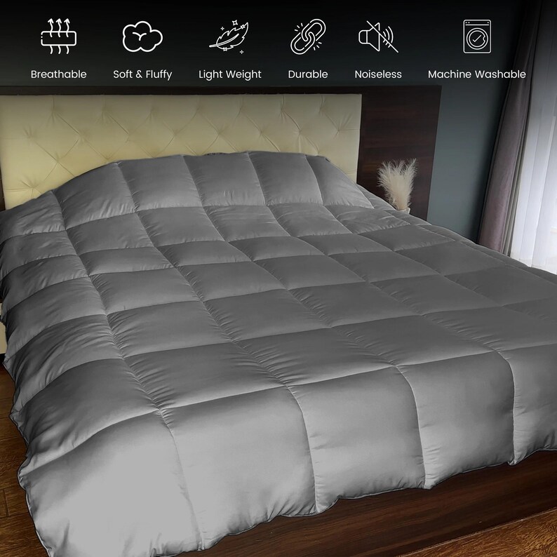 Op de afbeelding: Een grijze, gewatteerde dekbedovertrek op een bed. De dekbedovertrek is gemaakt van een zacht, donzig materiaal en is lichtgewicht. De dekbedovertrek is ademend, duurzaam en machinewasbaar. Het bed heeft een beige hoofdbord en staat in een slaapkamer.