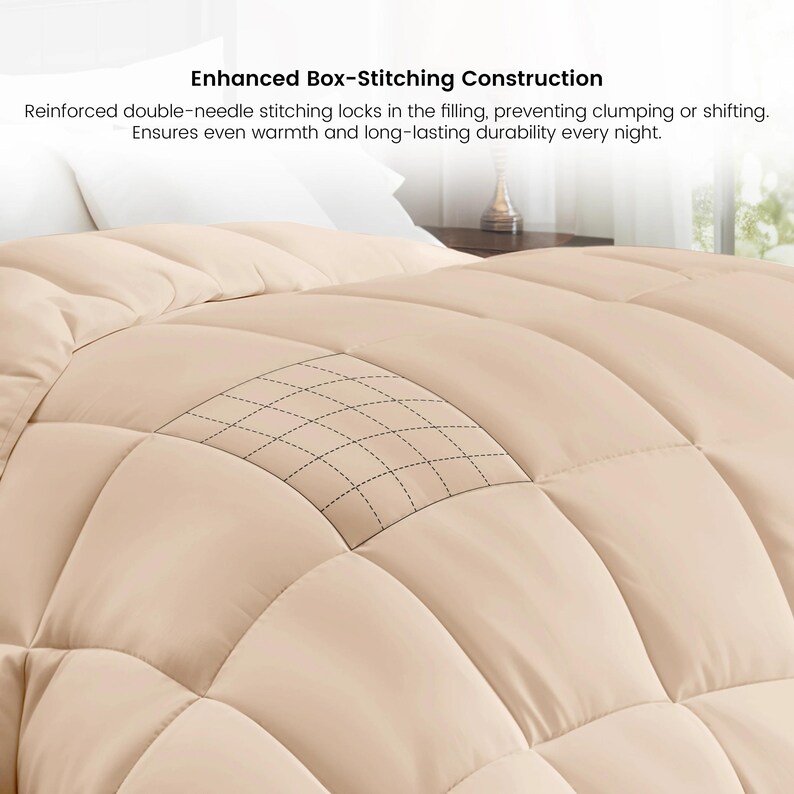 Op de afbeelding: Een close-up van een beige dekbed met een box-stitch ontwerp. Het dekbed heeft een rasterachtig stikselpatroon. De tekst "Enhanced Box-Stitching Construction" is zichtbaar.