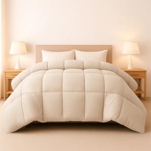 Op de afbeelding: Een beige dekbed op een bed met twee witte kussens. Het dekbed heeft een gewatteerd ontwerp. Twee bijpassende nachtkastjes met lampen staan aan weerszijden van het bed. De kamer heeft een neutraal kleurenschema.
