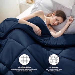 Op de afbeelding: Een marineblauwe quilt met een gewatteerd patroon. Het ligt op een bed met grijze kussens. De tekst op de afbeelding luidt "Microfiber Filling" en "All Seasons".