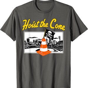 May include: Dark gray t-shirt with a graphic featuring an orange and white traffic cone with a skull and crossbones flag, set against a cityscape. The text "Hoist the Cone" is in yellow above the graphic.