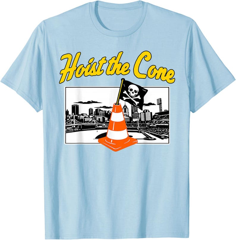 May include: Light blue t-shirt with the text "Hoist the Cone" in yellow. The graphic features an orange and white traffic cone with a skull and crossbones flag in front of a city skyline.